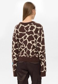 Un pull marron et beige avec un imprimé girafe, texture tricotée, col et poignets côtelés. Le design a une coupe légèrement courte et des manches longues.