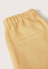 Tissu léger jaune avec une taille élastique froncée et une poche arrière. Texture lisse, design simple et coupe décontractée.