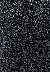 Tissu noir avec un motif texturé et des détails en paillettes argentées, créant une légère brillance sur la surface.