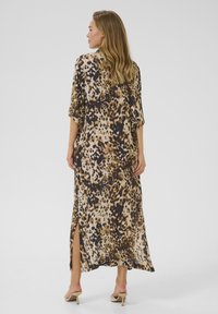 Vestito maxi con stampa animale, maniche corte, spacchi laterali, texture morbida e tonalità terrose di beige, marrone e nero. Sandali con tacco alto visibili.