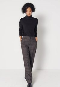 Czarny sweter z golfem, dopasowany; spodnie w wysokim stanie w kratkę w odcieniach brązu i szarości; kieszenie z przodu; zapięcie na dwa guziki.