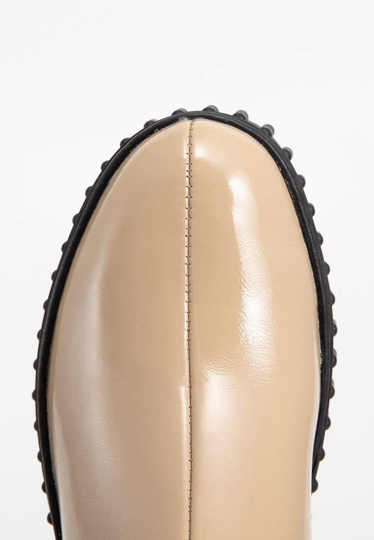 Stivale in gomma beige lucida con punta tonda, caratterizzato da una suola nera testurizzata e cuciture visibili lungo il centro.