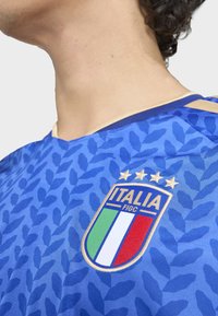 Blå fotbollströja med ett strukturerat mönster, med en guldtrimmad halsringning och en broderad Italiensk vapen med tre stjärnor.