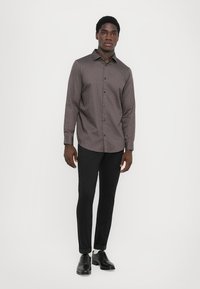 Grå mønstret skjorte med spredd krage, kombinert med svarte slim-fit bukser og svarte sko. Teksturen er glatt, med et subtilt design.