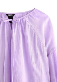 Blusa lavanda con scollo rotondo, dettaglio a fiocco e texture plissettata. Presenta un tessuto morbido e leggero e maniche dal taglio rilassato.