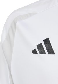 Maglietta atletica bianca con logo Adidas nero testurizzato sul lato superiore destro. Presenta un tessuto liscio e dettagli in mesh ventilato.