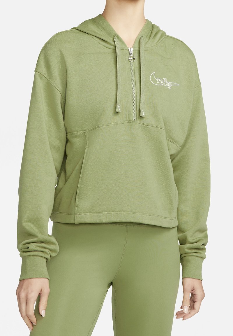 Personne portant un sweat à capuche court vert clair avec fermeture éclair frontale et cordons, associé à un legging vert assorti.