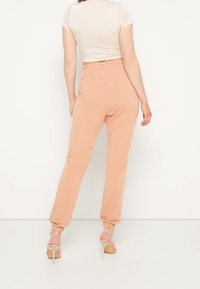 Růžové jogger kalhoty s elastickým pasem a manžetami na kotnících, vyrobené z jemné tkaniny s hladkým povrchem. Modelka má na sobě přiléhavý smetanový top.