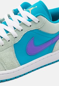 Baskets Nike avec une tige en cuir turquoise, des accents en daim gris, un swoosh Nike violet et des lacets blancs sur une semelle intermédiaire blanche.