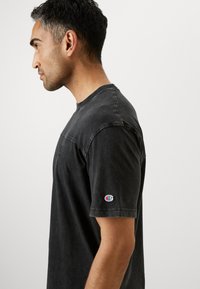 Schwarzes Baumwoll-T-Shirt mit Rundhalsausschnitt, kurzen Ärmeln und einem kleinen gestickten Logo am linken Ärmel. Klassische Passform mit subtiler Textur.
