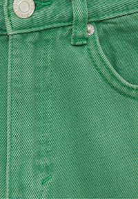 Tissu en denim vert avec une texture lisse, des coutures visibles et une poche avant ornée d'un bouton argenté.