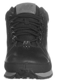 Chaussure de randonnée noire en cuir et en mesh, avec un bout arrondi, des lacets texturés et une semelle extérieure en caoutchouc visible. Logo positionné sur la languette.