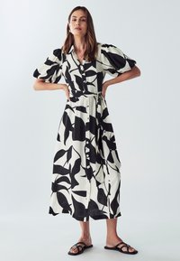 Schwarz-weiß gemustertes Midi-Kleid mit kurzen Puffärmel, Knopfverschluss und Taillengürtel. Glatte Stoffqualität mit einem Blattdesign.