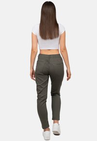 Olivgrüne Slim-Fit-Hosen mit einem elastischen Bund, zwei Gesäßtaschen und weißen Sneakers. Das Model trägt ein weißes Cropped-Top.