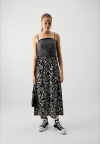 Denim top kleita ar sudraba rotājumiem, plūstoša melnbalta ziedu svārku daļa, apvienota ar melniem sporta apaviem un turētā melna soma.