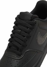 Zwarte leren Nike-sneaker met een getextureerd swoosh-logo, gevoerde kraag en zwarte geweven veters die in een kruislingse patroon zijn gestrikt.