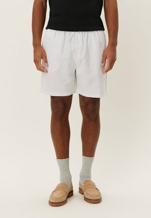 Hellgraue Leinen-Shorts mit einem elastischen Bund und Kordelzug, knielang, kombiniert mit beigen Slippern und grauen Socken.