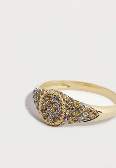 Prsteň so zlatistým tónom, ktorý má textúrovaný oválny dizajn s kovovými akcentmi a vsadenými žltými a priehľadnými drahokamami. Hladký pásik prsteňa.