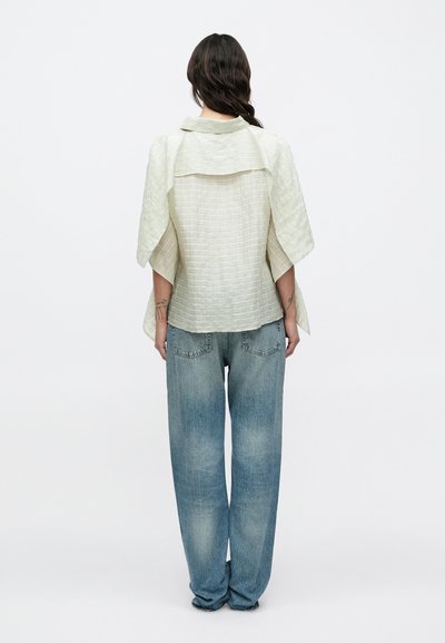 Ανοιχτό πράσινο λινό μπλουζάκι με υφή και φαρδιές μανίκια, συνδυασμένο με φαρδιά, ξεβάμμένα μπλε τζιν παντελόνια με πεντάτσεπη σχεδίαση.