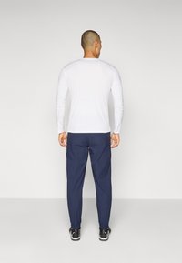 Langærmet hvid skjorte parret med marineblå bukser, der har elastisk talje og manchetter, subtil tekstur og sorte sneakers.