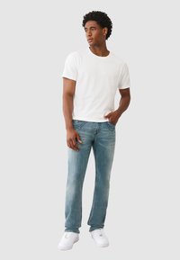 Biała bawełniana koszulka, średni fason. Jasnoniebieskie dżinsy z wyblakłą strukturą, proste nogawki. Białe trampki z sznurowanym zapięciem.