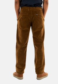 Bruine corduroy broek met een rechte pasvorm, voorzien van twee achterzakken en een klein logo-label op de rechterzak. Gladde textuur.