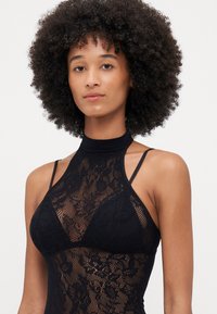 Bodysuit de renda preta com gola alta, alças finas e padrão floral. Textura transparente com forro sólido para cobertura. Design ajustado ao corpo.