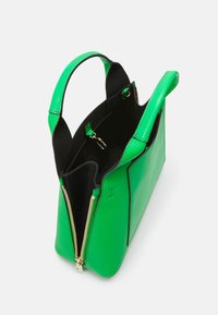 Zelená kožená kabelka s černými detaily, horními rukojetmi, zipovým uzávěrem a texturovaným exteriérem. Interiér má dvojité oddíly.