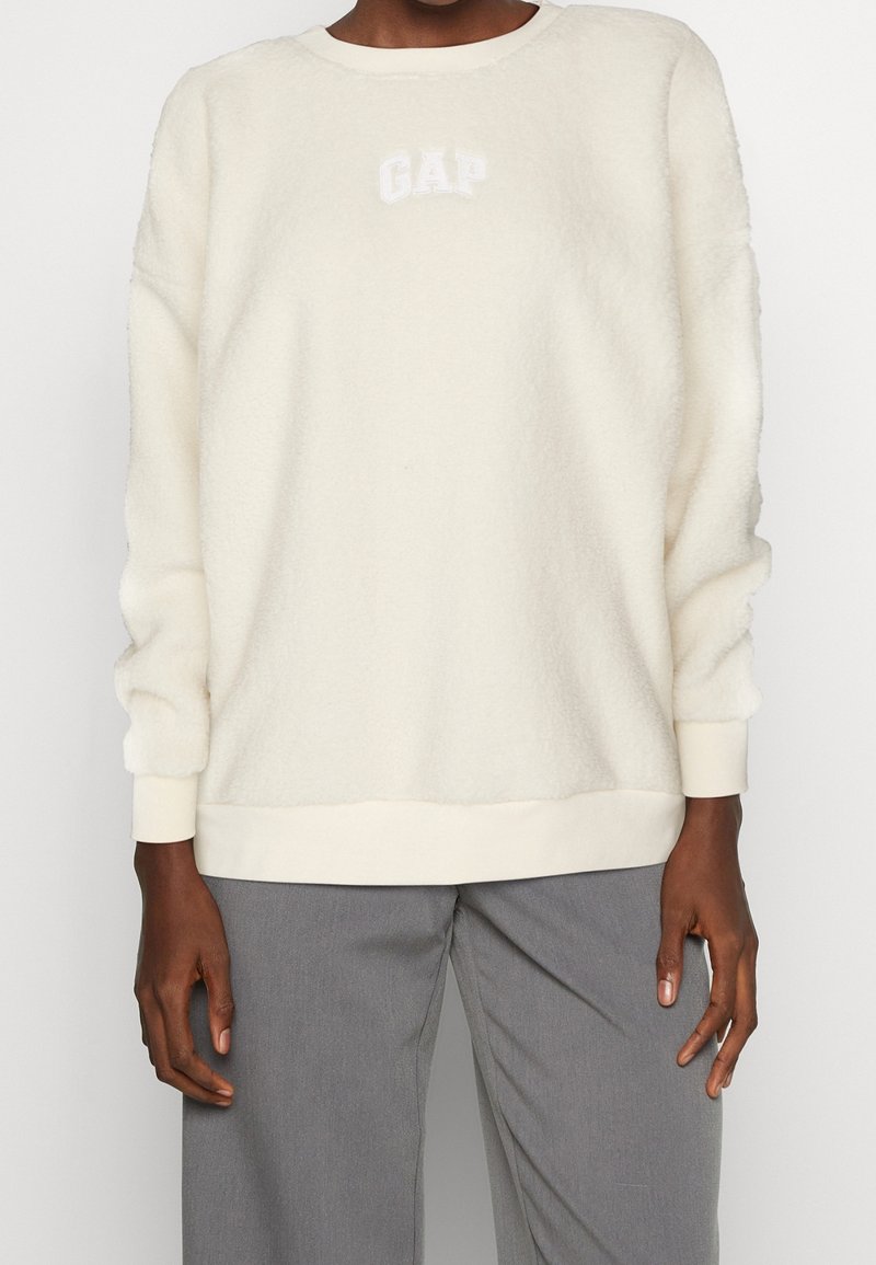 Polarowa bluza w kolorze kremowym, z okrągłym dekoltem, ściągaczami na mankietach i u dołu; na piersi znajduje się haftowane logo "GAP" w kolorze białym.