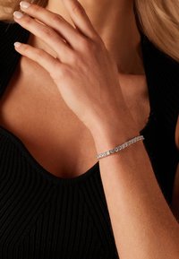 Zilveren armband met heldere edelstenen, met een elegante, slanke vormgeving. Draagt comfortabel om een pols, accentueert door textuur van zwarte stof.