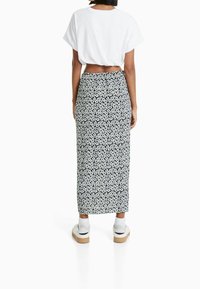 Maxi-Rock mit schwarzem Grund und weißem Blumenmuster, kombiniert mit einem weißen, kurz geschnittenen T-Shirt und weißen Sneakers. Glatte Textur, hohe Taillierung.