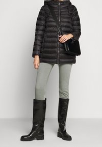 Černá prošívaná bunda s kapucí, zipem, žebrovanou texturou, doplněná zelenými úzkými džíny a černými koženými kozačkami ke kolenům. Součástí je černá kabelka.