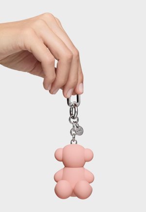 Hand holding a silver keyring attached to a soft pink teddy bear-shaped keychain against a plain white background.