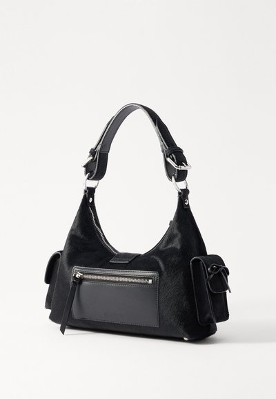 Sort håndtaske med en struktureret, pelslignende overflade, flad lynlåslomme på fronten, enkelt skulderrem og sidelomme med en bindedetalje.