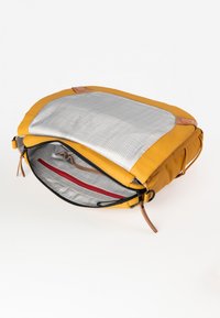 Borsa in pelle gialla con chiusura a zip, dotata di un interno a quadri grigi e una tasca di accento rossa. Accenti in pelle color cuoio vicino alla zip.