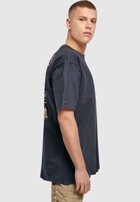 Tricou din bumbac gri închis, cu mâneci scurte, cu un fit lejer. Partea din față are un text și un design grafic. Textură netedă și decolteu clasic la gât.