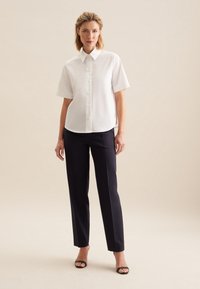 Hvid kortærmet knapop blouse med spids krave, kombineret med mørke, slim-fit bukser og sorte åbne stilethæle. Enkelt design, glat tekstur.