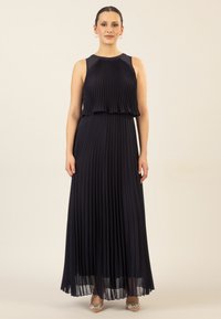 Navy pleated maxi-mekko, jossa on hihaton muotoilu, kerroksellinen vartalo ja valuva rakenne, täydentäen metallikoristeisia kenkiä.