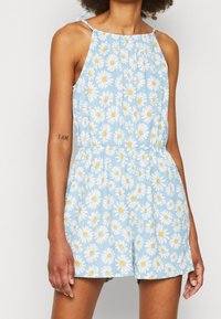 Jumpsuit floral azul con margaritas blancas y centros amarillos. Presenta tirantes finos, cuello recogido y una cintura elástica.