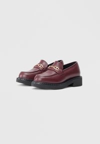 Burgundy läderloafers med guldkedjeaccent, låg plattform av svart gummisula, sydda detaljer och klassisk mokkasindesign.