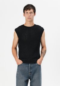 Sort ærmeløs strikket top med vertikal ribstrikstrukturer, rund hals og afslappet pasform. Sammen med lys blå denimjeans.