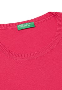 Světlý růžový bavlněný tričko s žebrovaným kulatým výstřihem. Obsahuje zelenou nálepku s nápisem "UNITED COLORS OF BENETTON." Hladká textura.