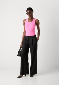 Tett rosa ribbestrikket tanktop, svarte vide bukser, svarte spisse hæler, liten teksturert svart veske, slanke solbriller. Minimalistisk stil.
