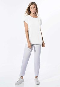 Witte t-shirt met korte mouwen en een brede halslijn, gecombineerd met lichtgrijze slim-fit broek en witte sneakers. Minimalistisch ontwerp, soepele textuur.