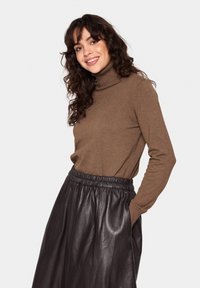 Brauner Rollkragenpullover aus weichem Stoff, kombiniert mit einem schwarzen Lederrock mit elastischem Bund und glatter, glänzender Texture.