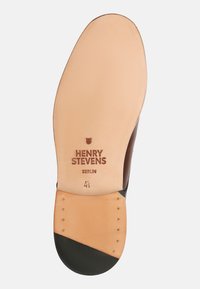 Semelle de chaussure en cuir avec un fond beige clair, un talon marron foncé, et le texte de marque "HENRY STEVENS BERLIN." Rivets visibles près du bord.