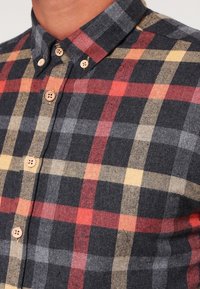 Camisa de franela con un patrón de cuadros en tonos grises, rojos, amarillos y negros; con botones en la parte delantera, cuello y botones de madera.