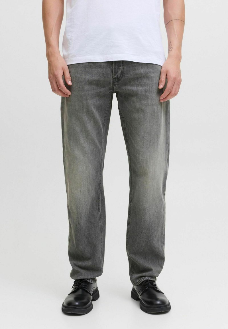 Jeans din denim gri deschis cu o croială dreaptă, prezentând urme ușoare de uzură, cinci buzunare și asortați cu pantofi negri.