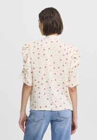 Pale yellow blouse with pink polka dots, puffed short sleeves, and a loose fit, made from lightweight fabric. Back view shown.