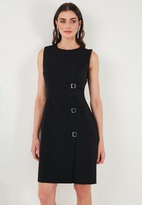 Black sleeveless dress with a fitted design, featuring three silver-tone buckle accents and a smooth, textured fabric.